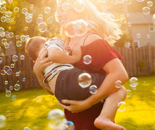 Woman carrying her son amidst floating bubbles