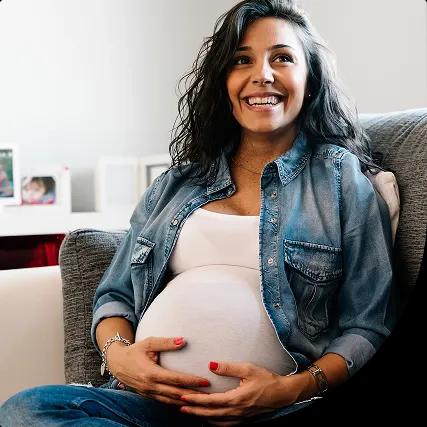 A smiling pregnant woman sits comfortably on a couch
